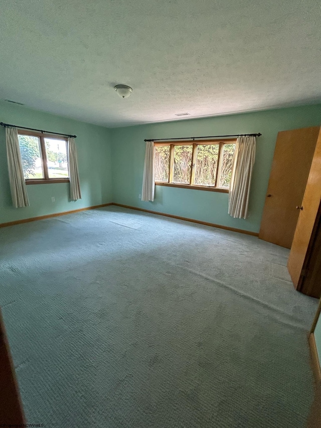 spare room featuring light carpet, a textured ceiling, and baseboards