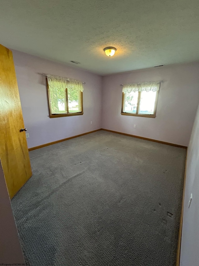 unfurnished room with carpet floors, visible vents, a textured ceiling, and baseboards