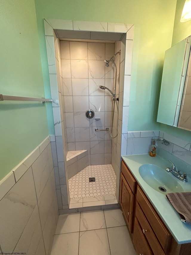 full bath featuring a wainscoted wall, a tile shower, vanity, and tile walls