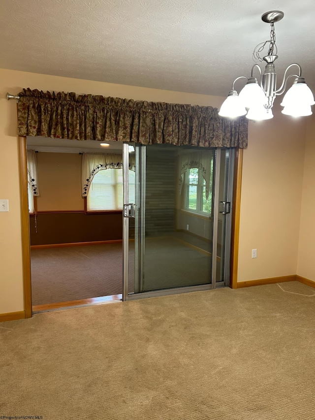 carpeted empty room with a notable chandelier, a textured ceiling, and baseboards