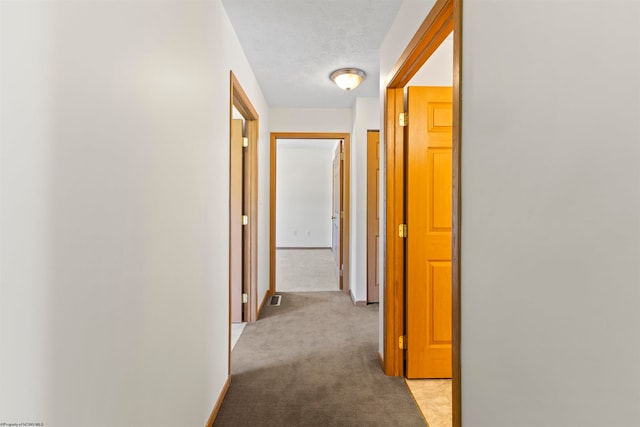 hall with a textured ceiling and light colored carpet