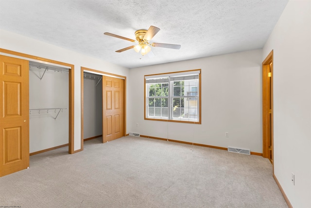 unfurnished bedroom featuring ceiling fan, two closets, light colored carpet, and a textured ceiling