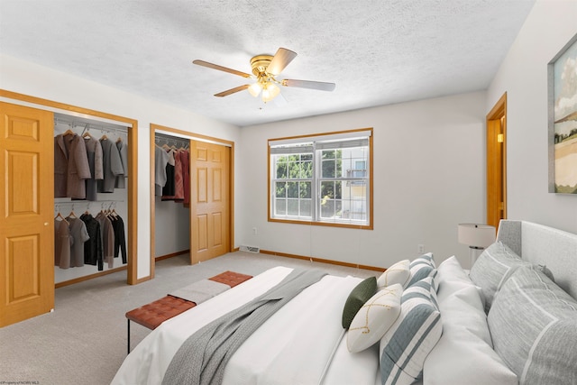 bedroom featuring ceiling fan, two closets, light colored carpet, and a textured ceiling