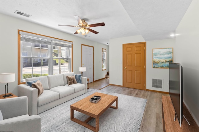 living room featuring ceiling fan, light hardwood / wood-style flooring, and a textured ceiling