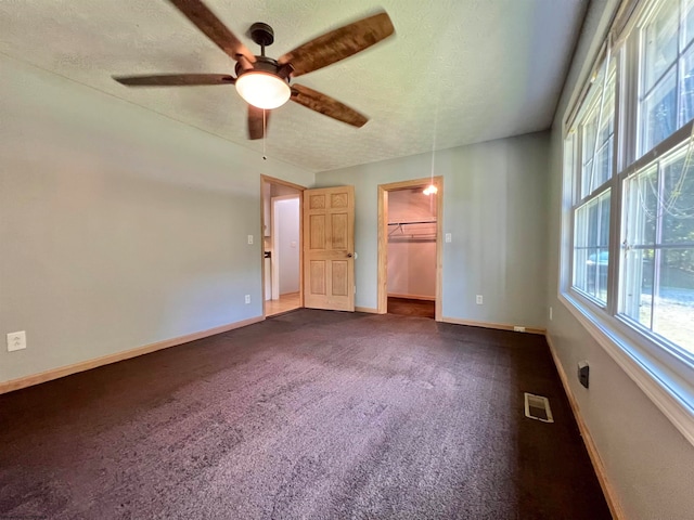 unfurnished bedroom featuring ceiling fan, dark colored carpet, a textured ceiling, a walk in closet, and a closet