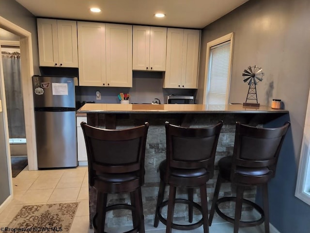 interior space featuring light tile patterned flooring, stainless steel refrigerator, and a kitchen breakfast bar