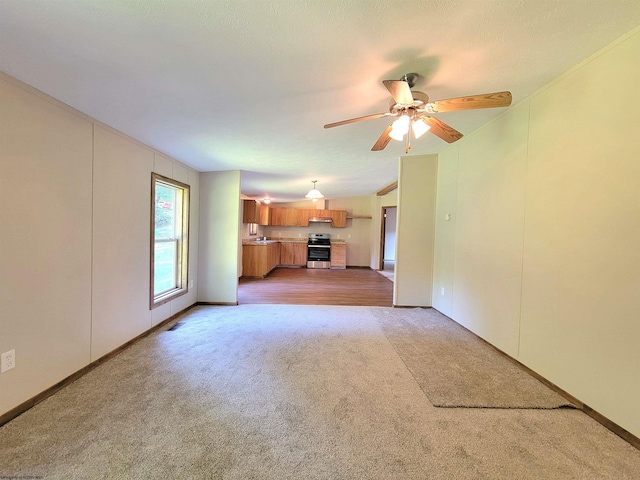 unfurnished living room featuring sink, ceiling fan, crown molding, and light colored carpet