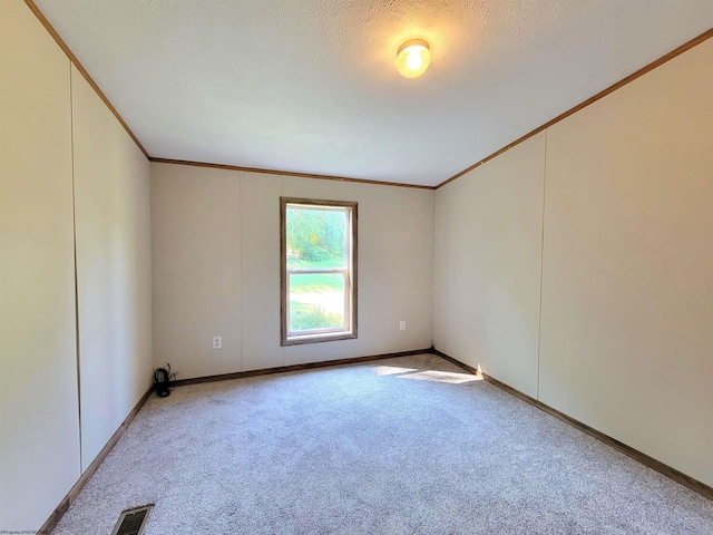 empty room with a textured ceiling, crown molding, and light colored carpet