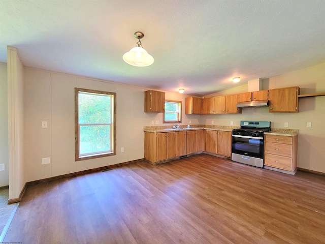 kitchen with under cabinet range hood, wood finished floors, light countertops, stainless steel range with gas stovetop, and pendant lighting