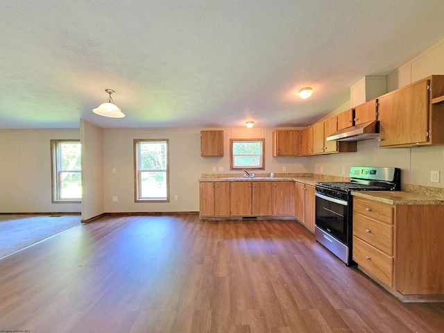 kitchen with light countertops, under cabinet range hood, pendant lighting, a wealth of natural light, and gas stove