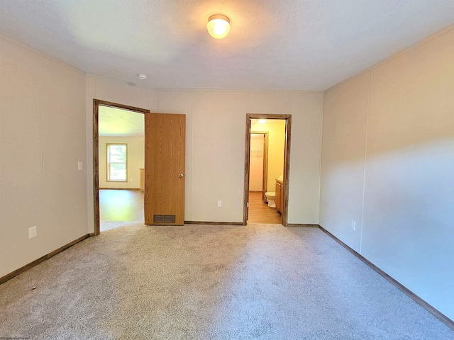 unfurnished bedroom featuring light carpet, a textured ceiling, ensuite bath, and baseboards