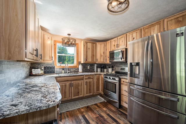 kitchen with a sink, hanging light fixtures, appliances with stainless steel finishes, dark stone countertops, and dark wood finished floors