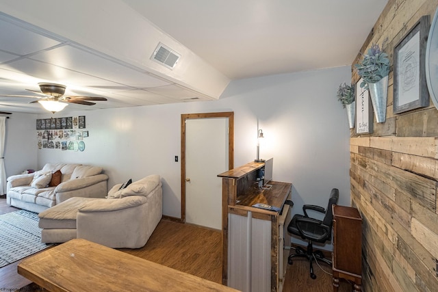 living room featuring a ceiling fan, visible vents, wood walls, and wood finished floors