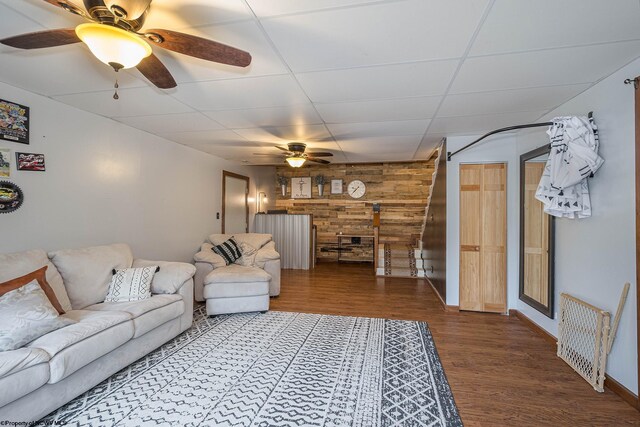 living room featuring ceiling fan, hardwood / wood-style flooring, a paneled ceiling, and wooden walls