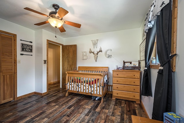 bedroom with dark wood-style floors, a nursery area, ceiling fan, and baseboards