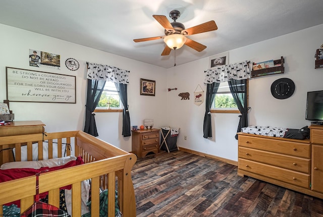 bedroom with ceiling fan, a crib, and dark hardwood / wood-style flooring