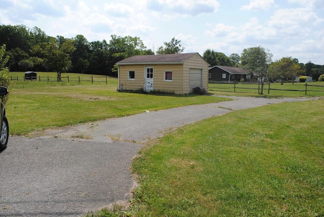 view of property exterior with a detached garage, fence, a lawn, and an outdoor structure