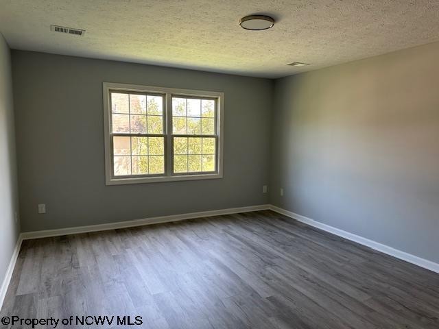 empty room with dark hardwood / wood-style flooring and a textured ceiling