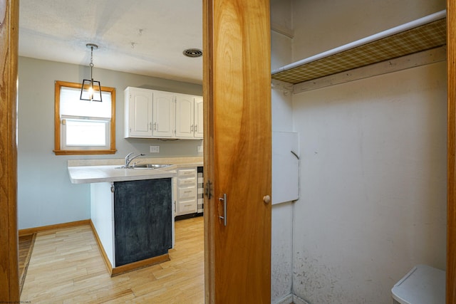 kitchen featuring decorative light fixtures, light hardwood / wood-style floors, white cabinetry, and sink