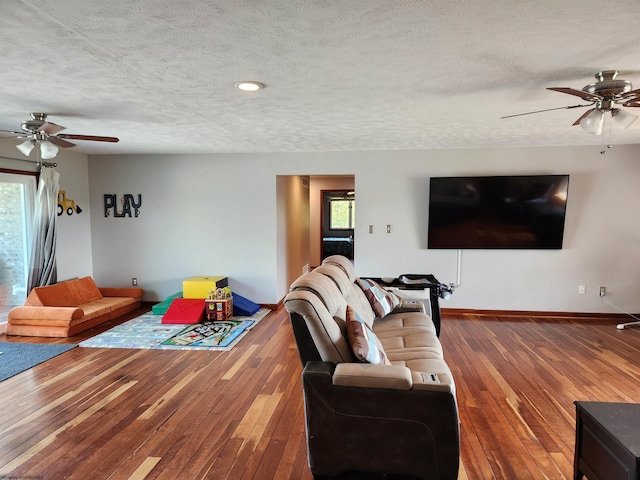 living room with ceiling fan, plenty of natural light, wood-type flooring, and a textured ceiling