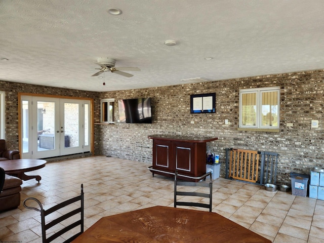 unfurnished living room with french doors, ceiling fan, brick wall, and a textured ceiling