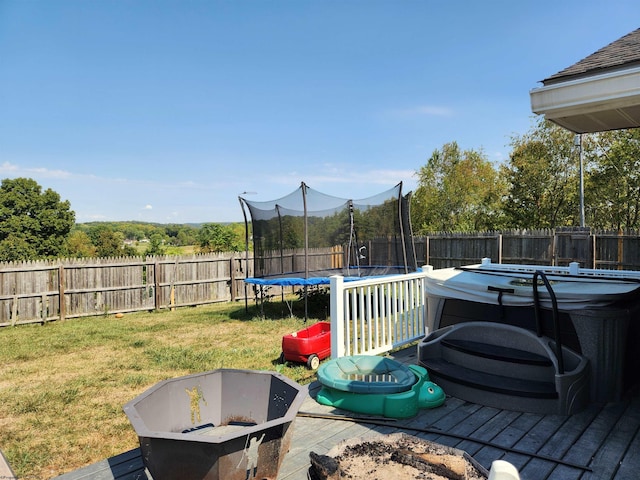 deck featuring a trampoline, an outdoor fire pit, and a lawn