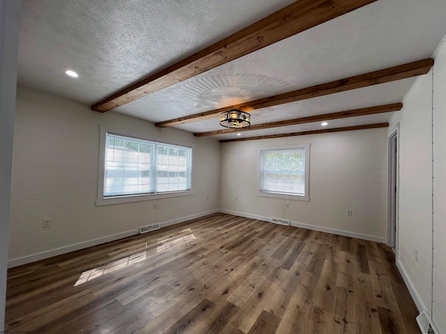 empty room featuring a textured ceiling, plenty of natural light, wood-type flooring, and beamed ceiling