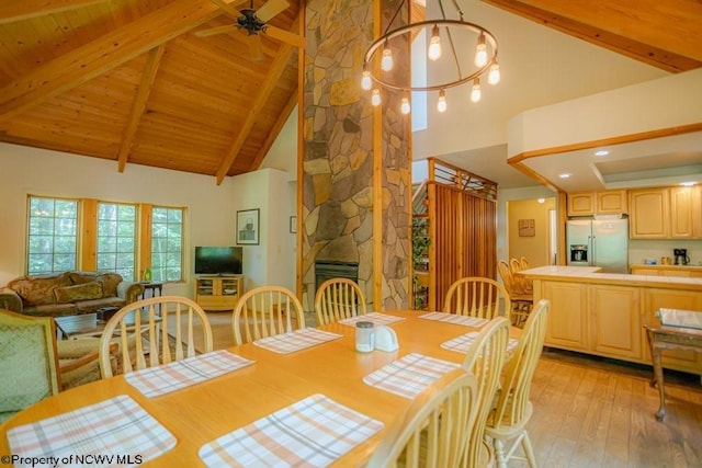 dining space with a fireplace, ceiling fan with notable chandelier, light hardwood / wood-style floors, beamed ceiling, and high vaulted ceiling