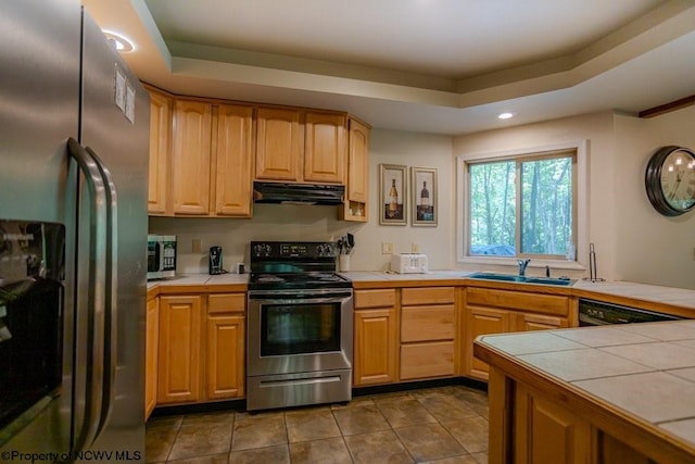 kitchen featuring a raised ceiling, sink, tile countertops, and appliances with stainless steel finishes