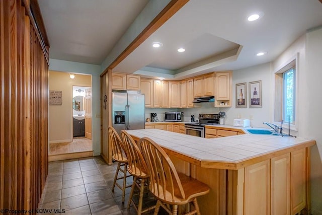 kitchen with stainless steel appliances, tile counters, kitchen peninsula, sink, and a breakfast bar area