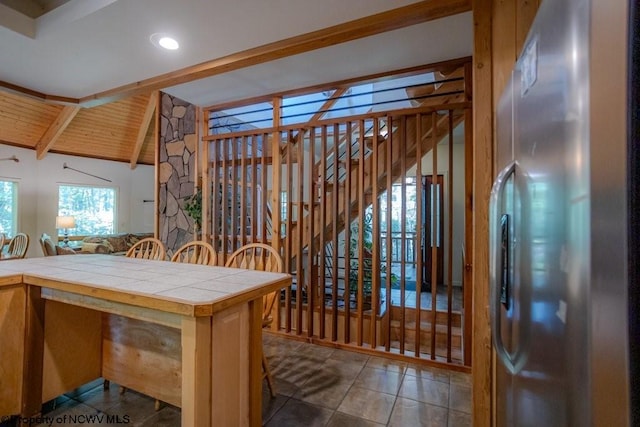 kitchen featuring stainless steel refrigerator, dark tile patterned flooring, tile countertops, vaulted ceiling with beams, and wooden ceiling