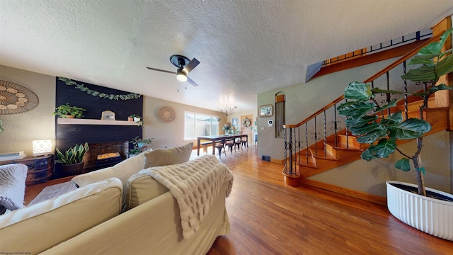 living room with a large fireplace, ceiling fan, wood-type flooring, and a textured ceiling