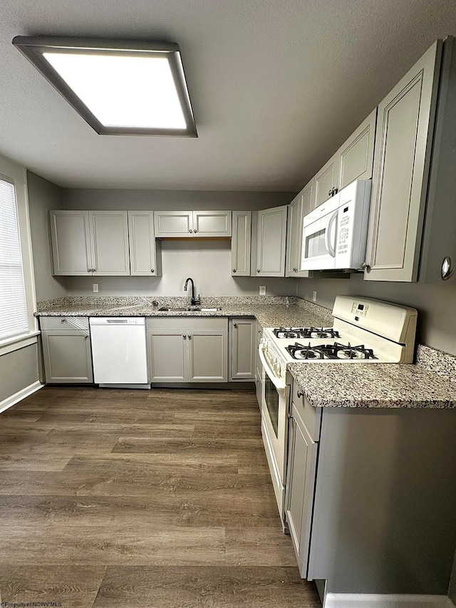 kitchen with dark hardwood / wood-style floors, white appliances, sink, gray cabinets, and light stone counters