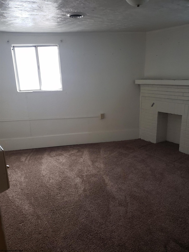 unfurnished living room featuring a textured ceiling, carpet, and a brick fireplace