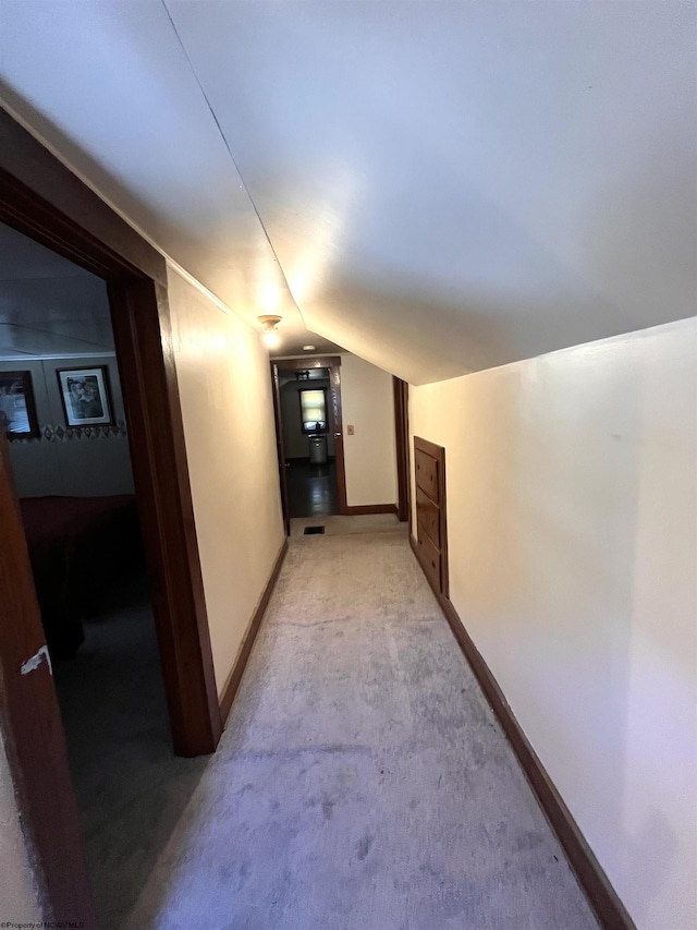 hallway with lofted ceiling, light carpet, and baseboards