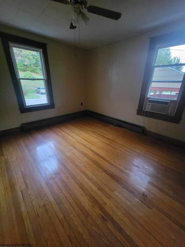 empty room featuring baseboards, hardwood / wood-style flooring, a baseboard radiator, ceiling fan, and cooling unit