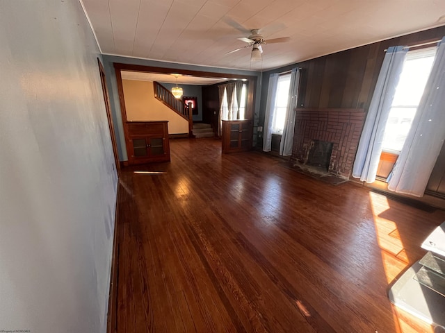 unfurnished living room featuring stairway, a fireplace, wood finished floors, and a ceiling fan