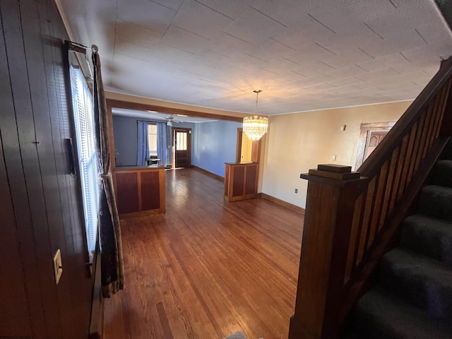 hall with a notable chandelier, wooden walls, wood finished floors, baseboards, and stairway