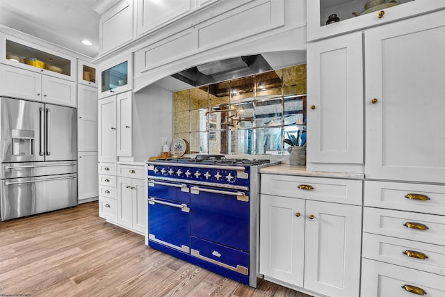 kitchen featuring light wood-type flooring, backsplash, premium range hood, appliances with stainless steel finishes, and white cabinets