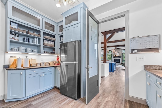 kitchen with a fireplace, beamed ceiling, stainless steel refrigerator, and light hardwood / wood-style floors