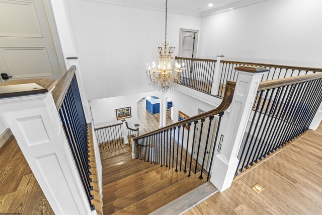 staircase with ornamental molding, hardwood / wood-style flooring, and a chandelier