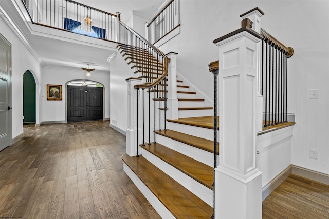 stairway with crown molding, wood-type flooring, and a high ceiling