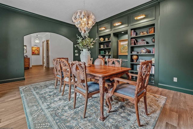 dining room featuring built in features, ornamental molding, light wood-type flooring, and a chandelier