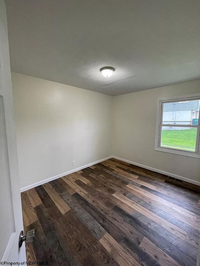 empty room with dark hardwood / wood-style floors and a textured ceiling