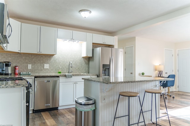 kitchen featuring white cabinets, stainless steel appliances, a kitchen island, and light stone countertops