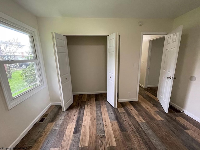 unfurnished bedroom featuring dark hardwood / wood-style flooring, a closet, and multiple windows