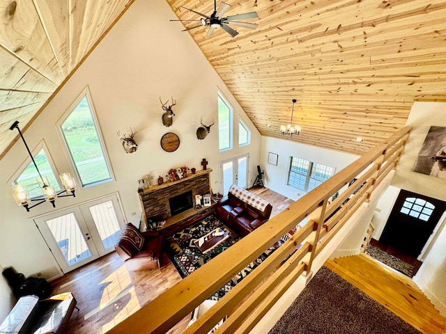 living room featuring high vaulted ceiling, ceiling fan with notable chandelier, wood-type flooring, a stone fireplace, and wood ceiling