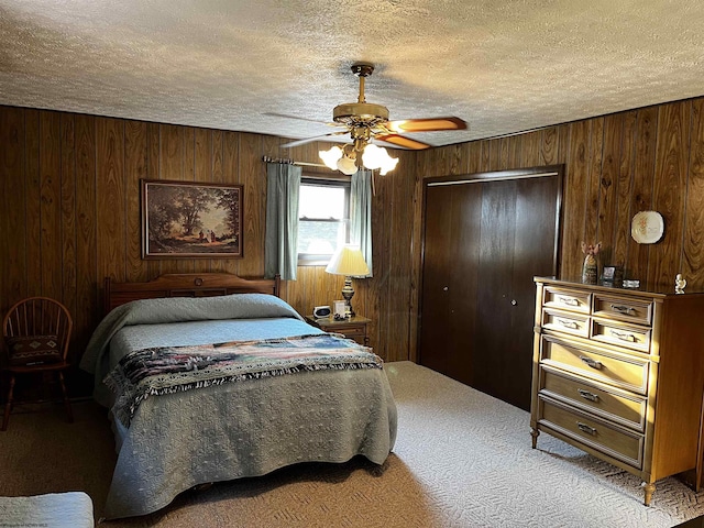 carpeted bedroom featuring a textured ceiling, ceiling fan, a closet, and wooden walls