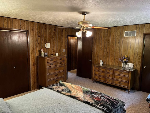 carpeted bedroom featuring a closet, ceiling fan, wooden walls, and a textured ceiling