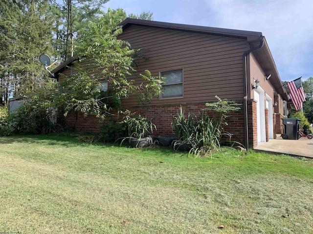 view of property exterior with brick siding, driveway, a garage, and a yard